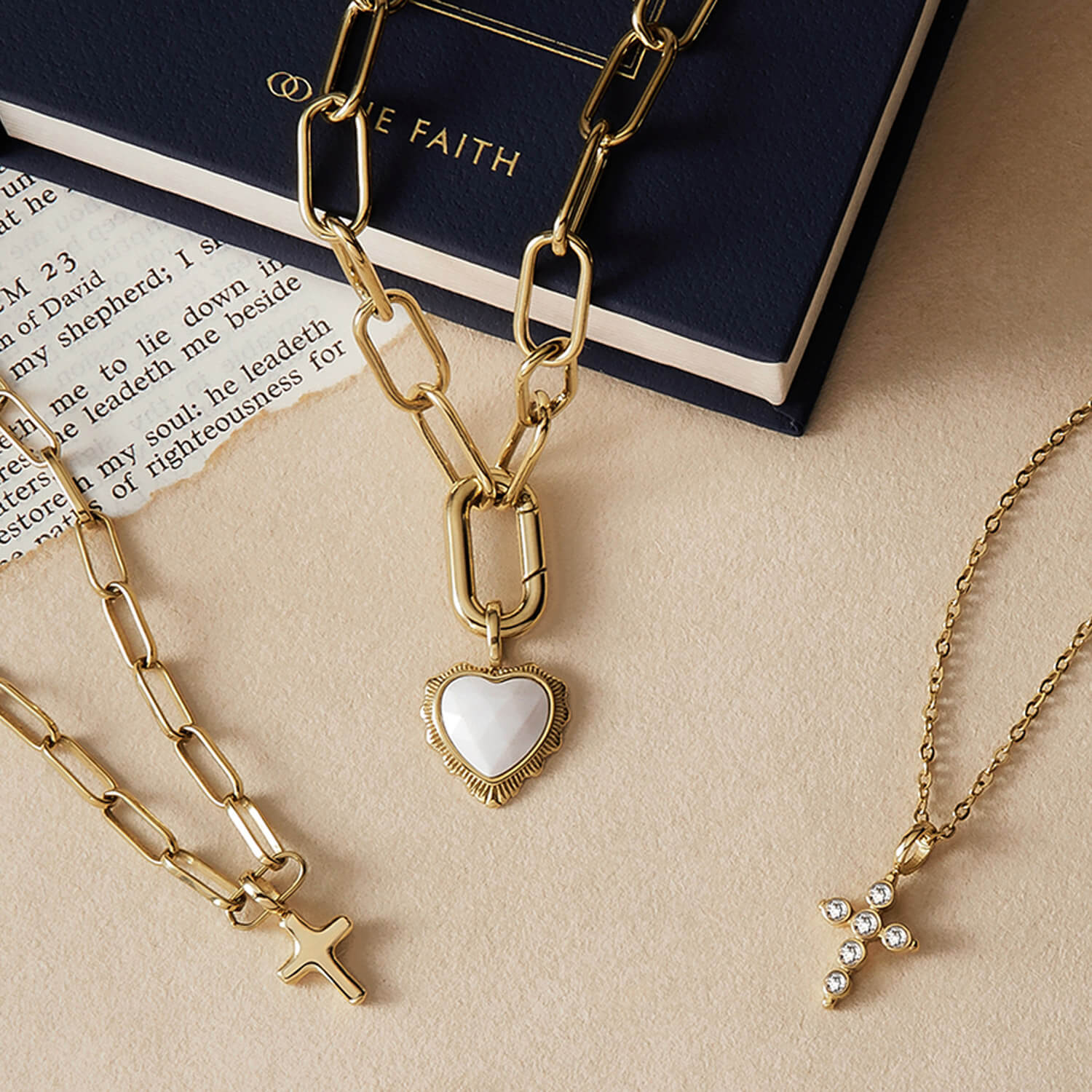 A styled flat-lay image of gold jewelry with The Faith's white onyx heart pendant necklace at the centre.
