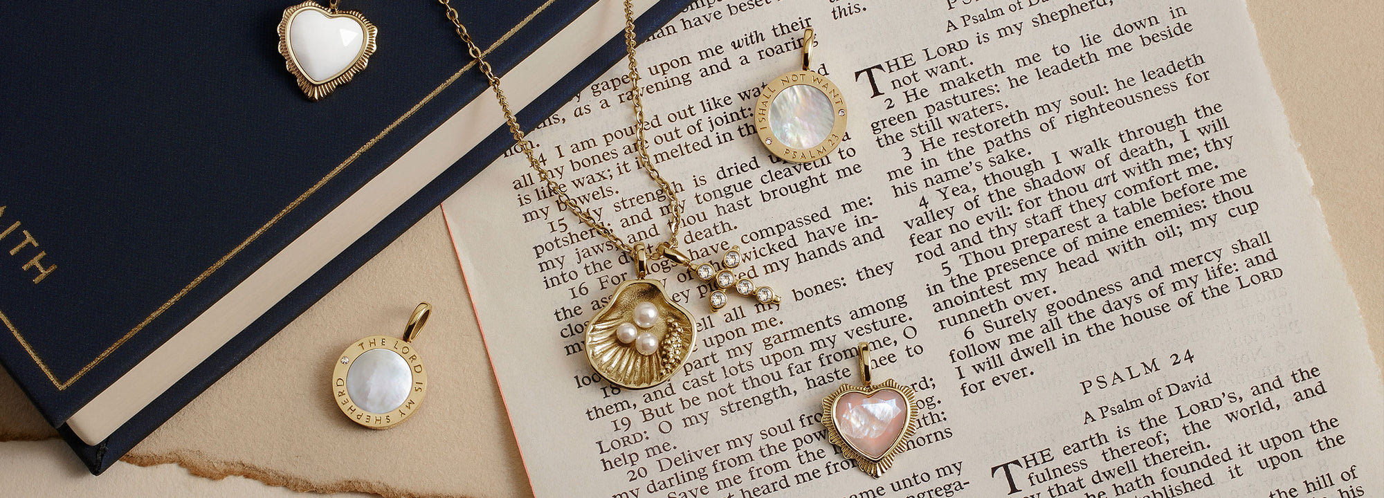 Gold-toned jewelry set including heart pendants, a shell pendant and two circle pendants with mother of pearl inlays, arranged on an open bible.